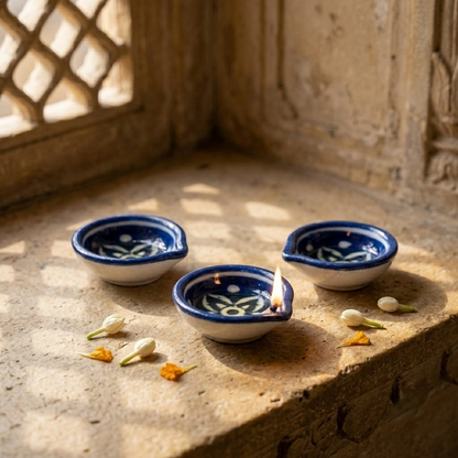 Three handcrafted Jaipur Blue Pottery diyas placed beside a rustic window in warm natural sunlight, minimal home décor styling