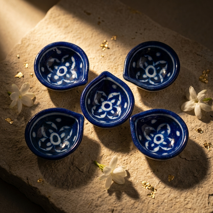 Five handcrafted Blue Pottery diyas arranged together with dramatic natural light highlighting white floral motifs