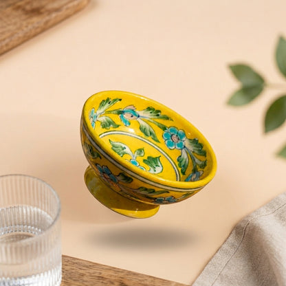 Handcrafted Jaipur Blue Pottery footed bowl in yellow displaying hand-painted blue floral and green vine motifs on a beige surface