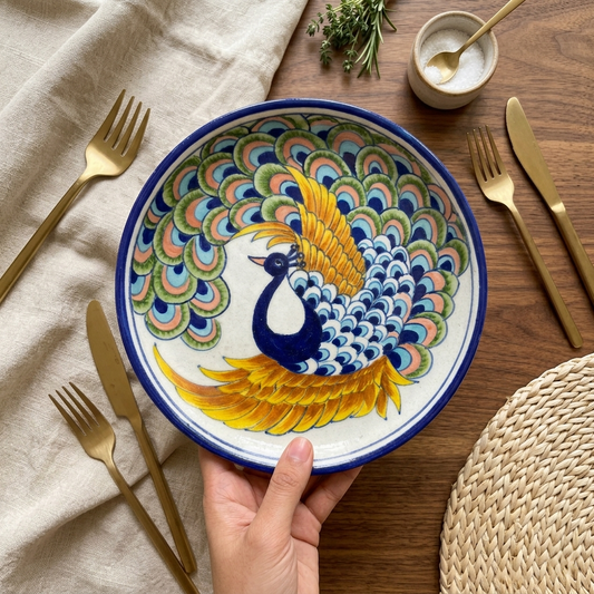 Artisan's hands placing a hand-painted Jaipur Blue Pottery peacock plate on a set dining table