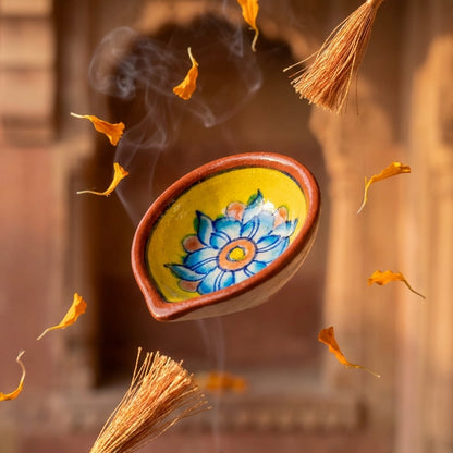 Lit Jaipur Blue Pottery oil lamp with a hand-painted blue lotus motif displayed in an arched niche for festive décor. 