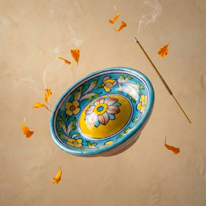 Jaipur Blue Pottery turquoise incense holder with smoke rising from a single agarbatti, marigold petals beside