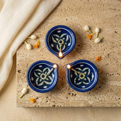 Three hand-painted Jaipur Blue Pottery diyas arranged in a floral clover pattern with delicate white flower petals