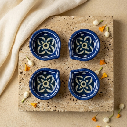 Set of four handcrafted Jaipur Blue Pottery diyas with white floral patterns arranged on a textured stone slab